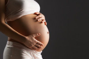 Pregnant woman caressing her belly over gray background